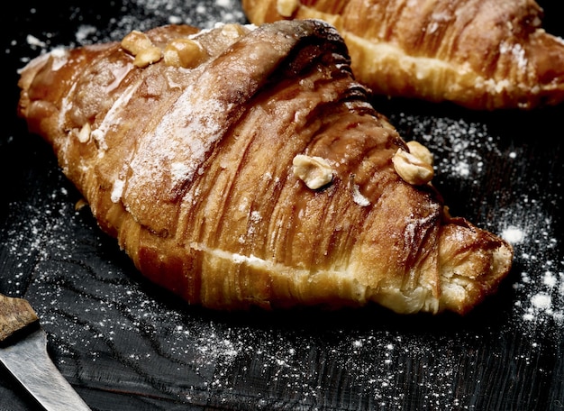 Gebackenes Croissant auf einem Holzbrett und mit Puderzucker bestreut schwarzer Tisch Appetitliches Gebäck zum Frühstück