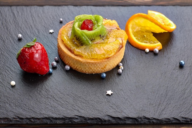 Gebackenes Dessert mit Kiwi-Orange und Erdbeeren auf schwarzem Stein