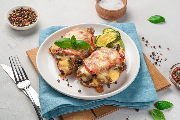 Gebackenes Fleisch mit Gemüse und Käse in einem weißen Teller auf grauem Hintergrund. Seitenansicht, Nahaufnahme.