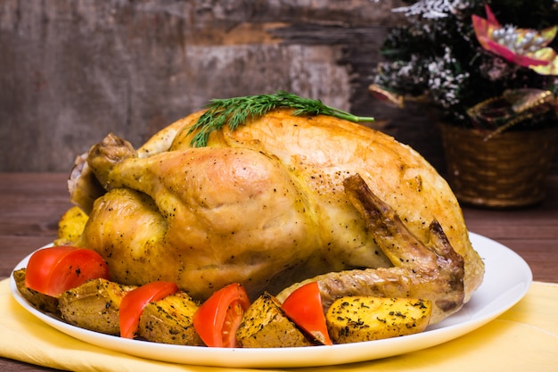 Gebackenes ganzes Huhn mit einer Beilage aus Kartoffeln und Tomaten auf einem Teller