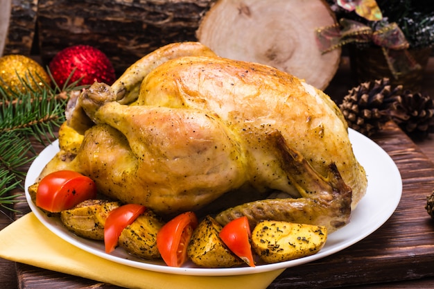 Gebackenes ganzes Huhn mit einer Beilage von Kartoffeln und Tomaten auf einer Platte, Weihnachtsdekoration