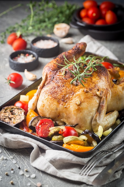 Gebackenes ganzes Huhn mit Gemüse und Kräutern Nahaufnahme auf einem Teller auf einem Tisch.