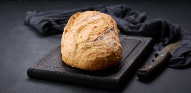 Gebackenes ganzes ovales Brot aus weißem Weizenmehl auf einem schwarzen Tisch