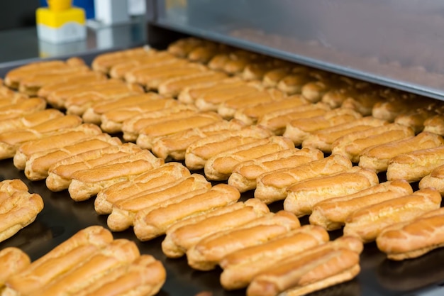 Gebackenes Gebäck auf Förderband Viele gelbe Eclair-Schalen Dessert aus natürlichen Zutaten Produkt für den Großhandel