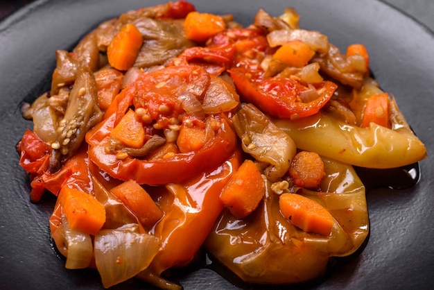 Gebackenes Gemüse, Auberginen, Paprika und Karotten auf einer schwarzen Platte auf konkretem Hintergrund