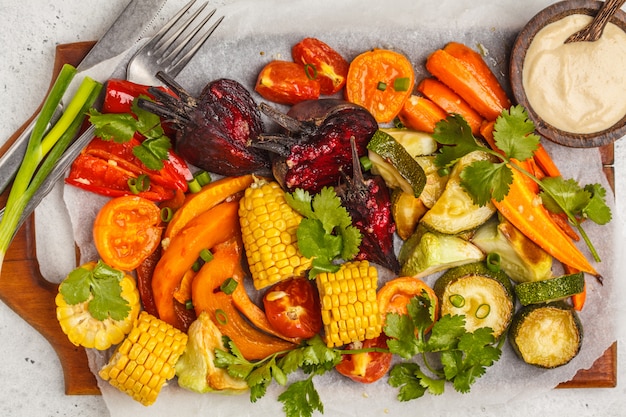 Gebackenes Gemüse: Kürbis, rote Rüben, Karotten, Paprika, Zucchini und Mais auf Holzbrett.