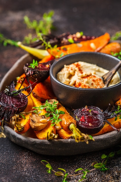 Gebackenes Gemüse mit Hummus in einem dunklen Teller.