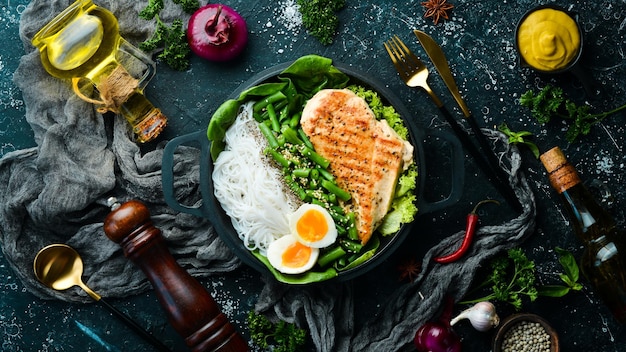 Gebackenes Hähnchenfilet mit Reisnudeln, Spinat und Bohnen in einer schwarzen Steinplatte Diätkost Draufsicht Freier Platz für Text