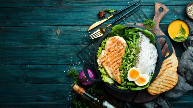 Gebackenes Hähnchenfilet mit Reisnudeln, Spinat und Bohnen in einer schwarzen Steinplatte Diätkost Draufsicht Freier Platz für Text