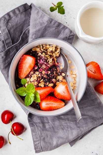 Gebackenes Hafermehl mit Beeren und Milch in einer grauen Schüssel, Draufsicht. Veganes Frühstück.