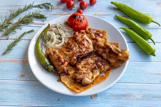 Gebackenes Hühnerschnitzel auf blauem Holzhintergrund mit gerösteten Tomaten, Zwiebeln und Paprika