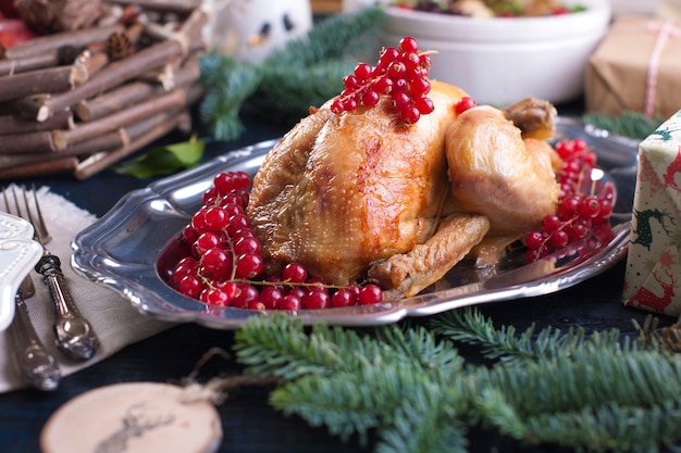 gebackenes Huhn auf einer Platte mit roten Beeren. auf einem blauen Holztisch mit einem Rechen