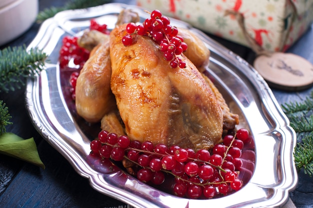 gebackenes Huhn auf einer Platte mit roten Beeren. auf einem blauen Holztisch mit einem Rechen