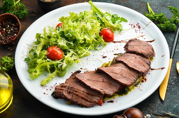 Gebackenes Kalbssteak mit Salat und Gemüse Auf schwarzem Hintergrund Draufsicht Rustikaler Stil