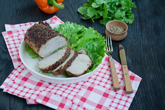 Gebackenes Schweinefilet in den Gewürzen geschnitten auf einer weißen Platte mit grünem Salat.