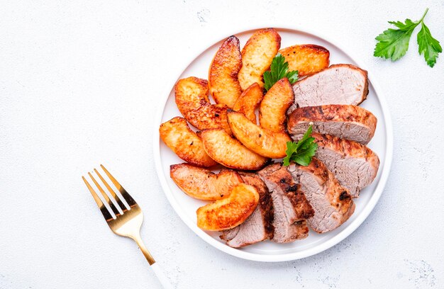 Gebackenes Schweinefilet mit Quitten- oder Apfelscheiben, serviert auf Platte Draufsicht auf weißen Tischhintergrund