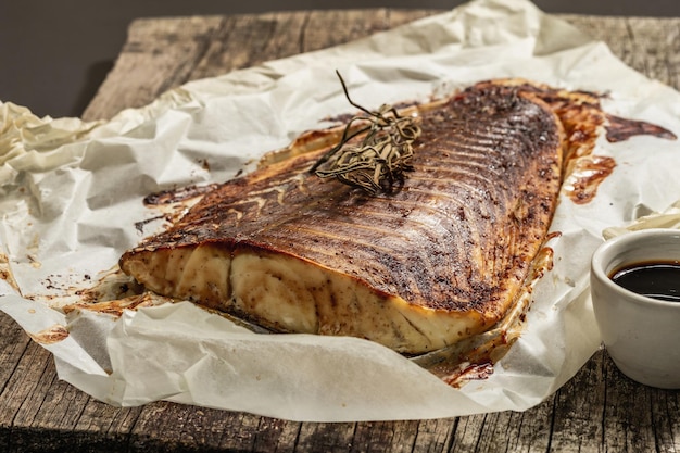 Gebackenes Seelachsfilet (Pollachius virens). Fisch mit Teriyaki-Sauce für einen gesunden Lebensstil. Rosmarin, Sojasauce, Pergament. Holzständer, schwarzer Steinbeton Hintergrund, Nahaufnahme