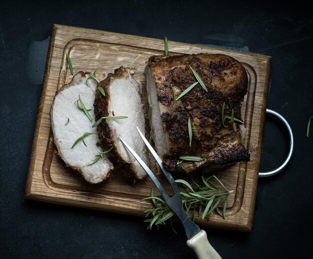 Gebackenes Stück Schweinefleisch in Gewürzen auf einem Holzbrett, in Stücke geschnitten. Auge des runden Bratensteaks