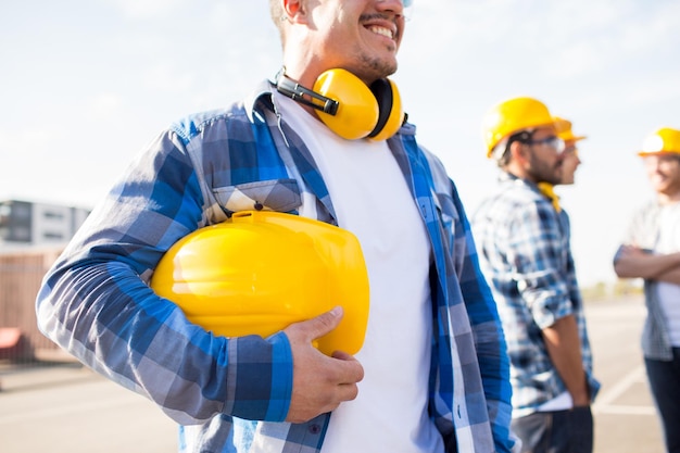 Gebäude-, Schutzausrüstungs- und Personenkonzept - Nahaufnahme des Bauarbeiters mit gelbem Hardhat oder Helm auf der Baustelle