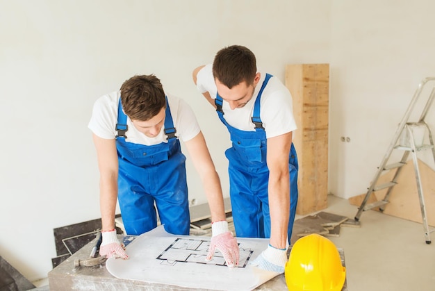 Gebäude, Teamwork und People-Konzept - Gruppe lächelnder Bauherren in Hardhats mit Blaupause im Innenbereich