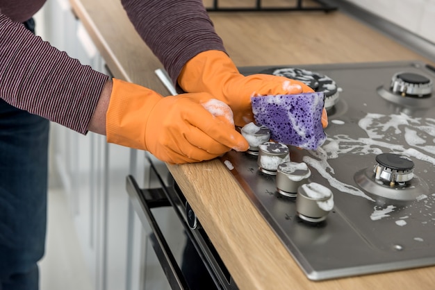 Geben Sie orangefarbene Schutzhandschuhe mit Küchenmöbeln zum Waschen und Sprühen von Lappen ab