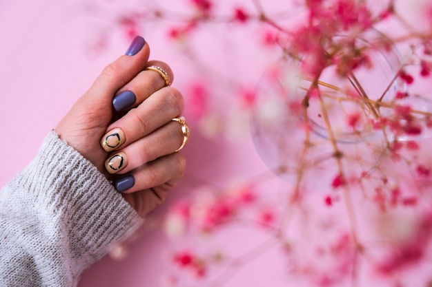 Geben Sie Pullover und rosa Blumen mit modernen Manikürenägeln ab. Weibliche Hand. Glamouröse schöne Maniküre. Maniküre-Salon-Konzept. Nagellack hautnah.