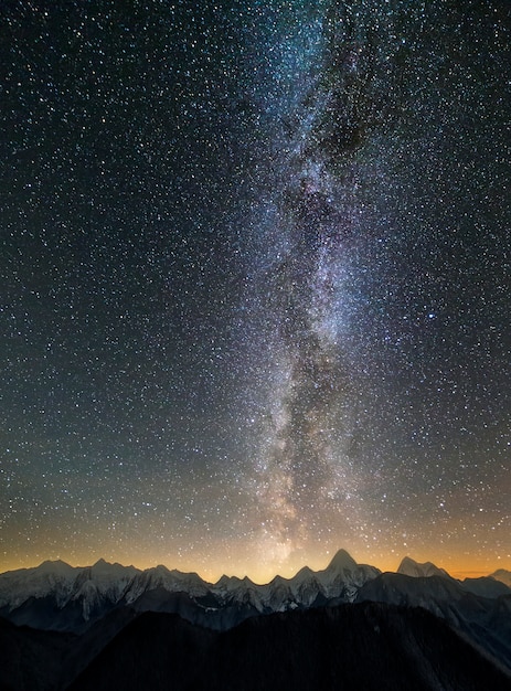 Gebirgswinter-Nachtpanoramalandschaft. Steile Berggipfel bedeckt mit Schnee und Fichtenwald, beleuchtet, indem man Sonnenhorizont unter dunkelblauem sternenklarem Himmel und heller Milchstraßenkonstellation einstellt.