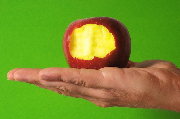 Gebissener roter Apfel zur Hand auf einem farbigen Hintergrund