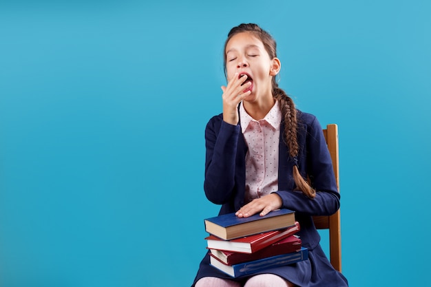 Foto gebohrtes müdes gähnendes schulmädchen in der uniform mit dem stapel von büchern sitzend auf stuhl, mangel an motivation, konzept zu studieren und zu lesen