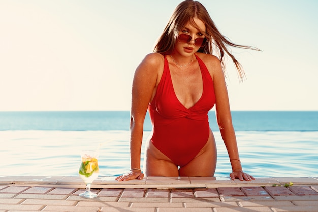 Foto gebräunte frau im roten bikini in einem pool mit cocktail