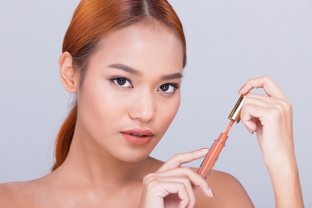 Gebräunte Haut junge Mode asiatisches Frauenmodell vorhanden, das kosmetische Make-up-Paketprodukte zeigt, leeren Kopienraum auf ihrer Handfläche, seitliche Rückansicht offene Schulter oben ohne, Studiobeleuchtungswerbung drehen