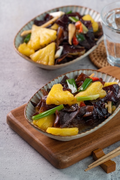 Gebratene Ananas mit schwarzem Holzohrpilz. Hausgemachtes leckeres Essen mit Schalotten auf grauer Tischoberfläche.
