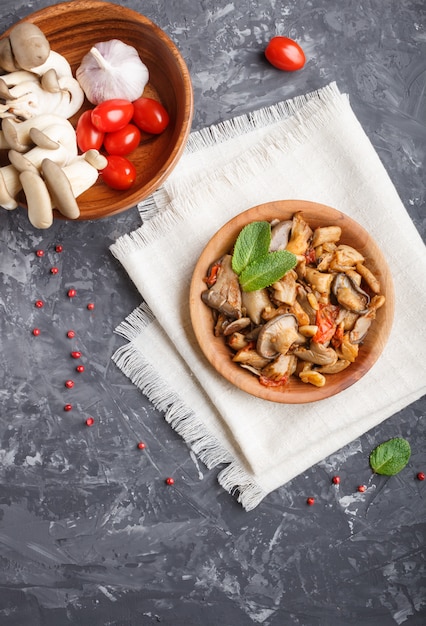 Gebratene Austernpilze mit Tomaten in der hölzernen Platte auf Schwarzem