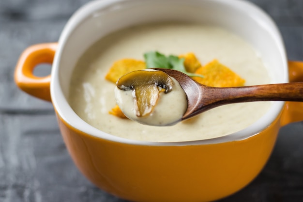 Gebratene Champignons in einem Holzlöffel über der Sahne der Wildpilzsuppe