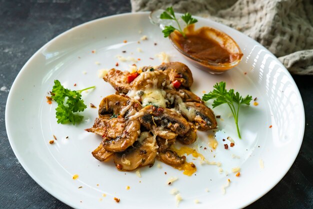 Gebratene Champignons mit Käsesauce in einem weißen Keramikteller mit Kräutern