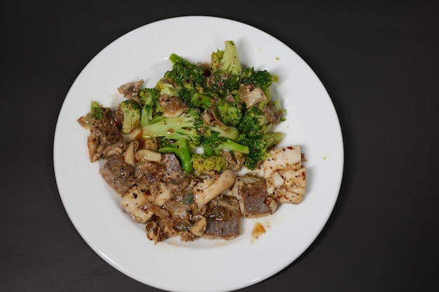 Gebratene Champignons mit Knoblauch und Petersilie auf einem schwarzen Teller auf weißem Hintergrund