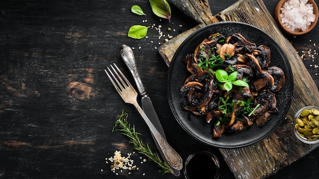 Gebratene Champignons mit Petersilie auf dem Teller auf schwarzem Hintergrund Ansicht von oben Freier Platz für Ihren Text