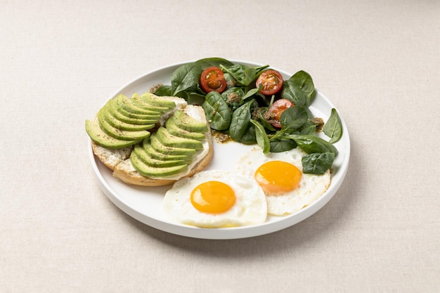 Gebratene Eier mit Avocado-Sandwich und Salat mit Kirschtomaten Gesundes Frühstück auf einem weißen Teller