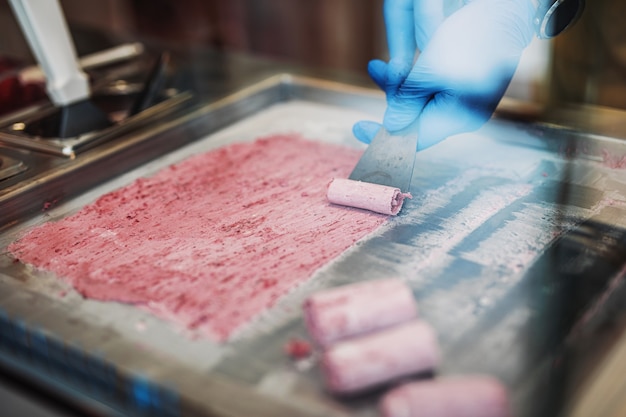 Gebratene Eiscremerollen an der Gefrierpfanne. Handgemachtes gerolltes Eisdessert auf kalter Platte. Gebratene Eismaschine mit gekühlter Stahlpfanne.