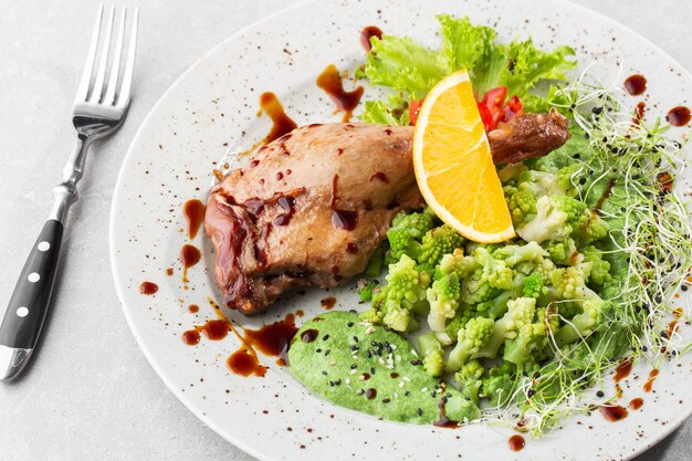 Gebratene Entenkeule mit gebackenem Romanesco-Brokkoli, Zitronenscheibe und Chili-Pfeffer auf weißem Teller