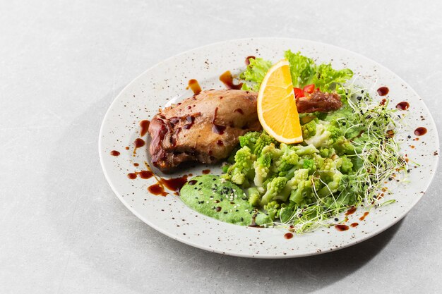 Gebratene Entenkeule mit gebackenem Romanesco-Brokkoli, Zitronenscheibe und Chili-Pfeffer auf weißem Teller