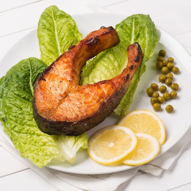 Gebratene Forelle mit einem Stück Salat Zitrone und grünen Erbsen