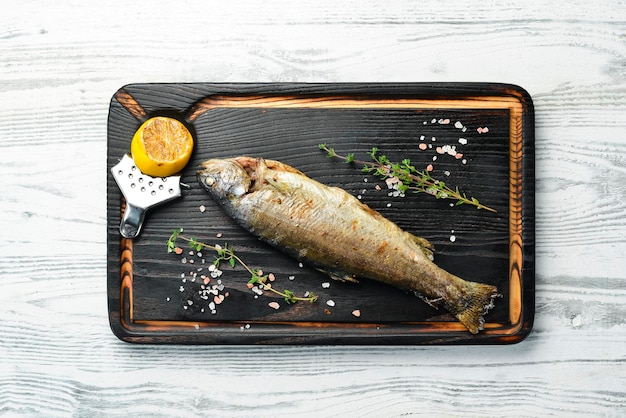 Gebratene Forelle mit Zitrone und Zwiebel auf einer hölzernen Tafel, Draufsicht