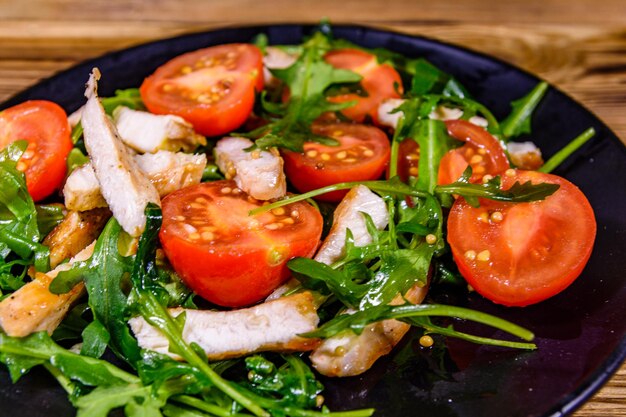 Gebratene Hähnchenbrust und Salat mit Rucola und Cherrytomaten in einem schwarzen Teller