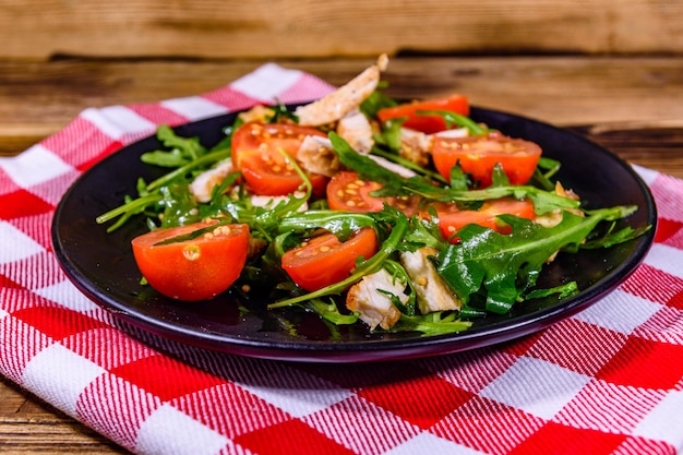 Gebratene Hähnchenbrust und Salat mit Rucola und Cherrytomaten in einem schwarzen Teller