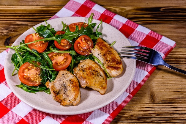 Gebratene Hähnchenbrust und Salat mit Rucola und Kirschtomaten in einem Keramikteller