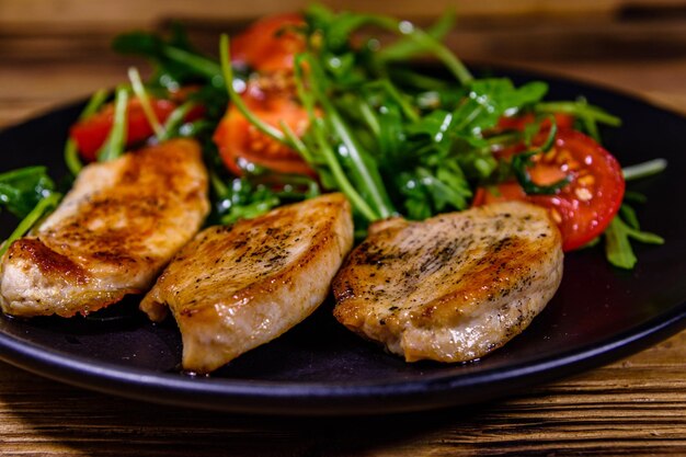 Gebratene Hähnchenbrust und Salat mit Rucola und Kirschtomaten in einem schwarzen Teller