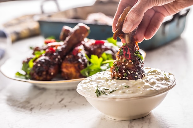 Gebratene Hähnchenschenkel in Frauenhand und Tzatziki-Dip-Sauce oder Dressing.