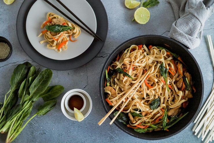 Gebratene hausgemachte vegetarische asiatische Nudeln mit Gemüse und Blattspinat in der Pfanne von oben