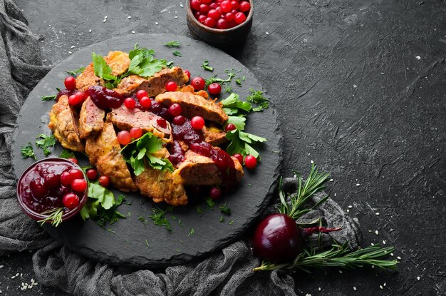 Gebratene Hühnerleber mit Preiselbeersauce und Preiselbeeren auf einer schwarzen Steinplatte. Rustikaler Stil. Ansicht von oben.